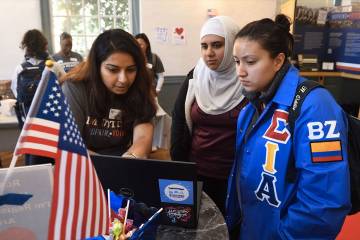 Three students look at a laptop computer during a voter registration event