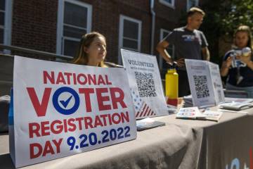 A young woman sits at a table with a sign that reads "National Voter Registration Day"